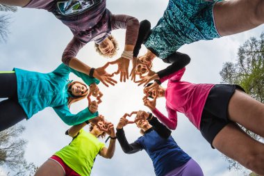 Bir grup kadın sporcu elleriyle kalp oluşturarak daireler çiziyor. Spor için barış ve sevgi mesajı. Farklı yaşlardaki kadınlar eğitimden sonra eğleniyorlar.