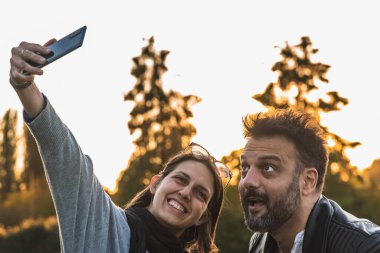 Gün batımında dışarıda komik yüzlü bir çift selfie çekiyor.