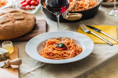 Domates soslu spagetti tabağına odaklanmış bir masa. Ekmek, çatal bıçak takımı ve arka planda bir bardak kırmızı şarap.