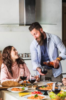 Mutlu arkadaşlar grubu restoranda kırmızı şarap içip makarnayla yemek yiyor. Gençler sosyalleşiyorlar, içiyorlar ve yemek yiyorlar. Şaraphane bar masasında oturuyorlar. Yemek yaşam tarzı konsepti