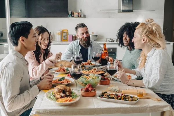 Happy group of friends having dinner party at home. Cheerful young people having lunch break together. Life style concept. Food and beverage lifestyle with spaghetti, italian pasta and red wine