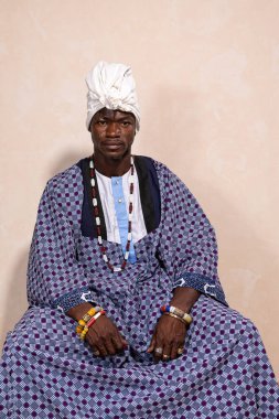 Genç Afrikalı bir adamın portresi, rastalı ve tipik renkli kıyafetler giymiş. Ciddi bir ifade ve kameraya bak.