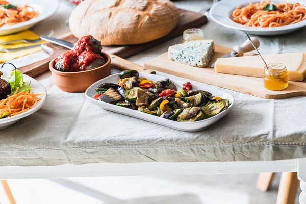 Bir tabak peynir ve reçelli masa seti, domates soslu spagetti, ızgara sebze. Odayı aydınlatan gün batımı ışığı