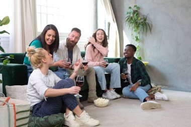 Arkadaşlar rahat bir oturma odasının etrafında rahatça otururlar ve rahatlıkla çevrelenmiş şarap kadehleri eşliğinde neşeli sohbetler ederler.