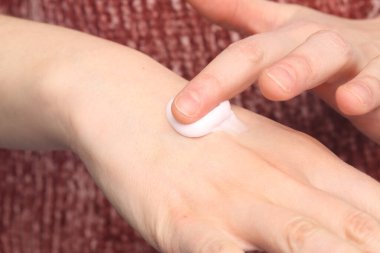 Kadının eli koluna nemlendirici krem sürerek cildini besliyor ve nemlendiriyor.