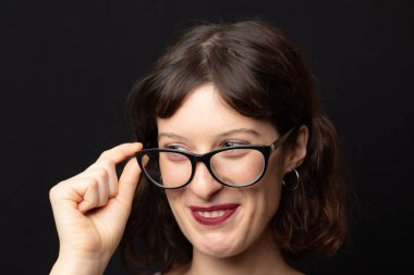 Çekici bir genç kadın siyah çerçeveli gözlüğünü şakayla ayarlıyor.