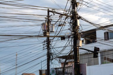 Şehrin karmaşık ve kaotik enerji altyapısını gözler önüne seren karmaşık elektrik kablolarından oluşan bir ağ kent direğini taçlandırıyor.