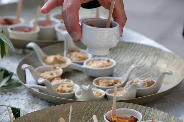 stock image Hand holding a white porcelain gravy boat over a variety of appetizers on a silver platter