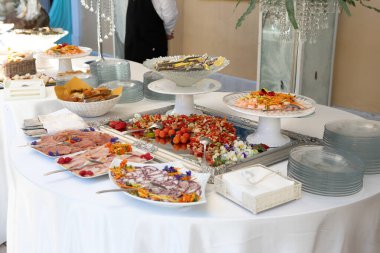 Büfe masasında yemek servisi sırasında çeşitli lezzetli yemekler sunuluyor. Arka planda bir garson duruyor.