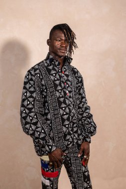 Bir fotoğraf stüdyosunda poz veren genç siyahi bir adam geleneksel Afrika kıyafetleri giyiyor.
