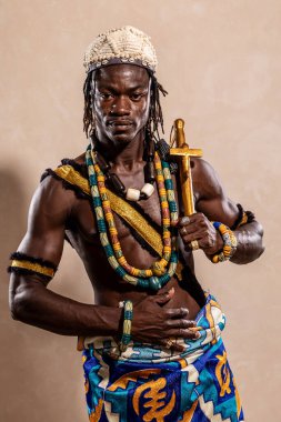 Renkli geleneksel kıyafetler ve aksesuarlar giyen Afrikalı kaslı savaşçı elinde altın bir silah tutuyor.