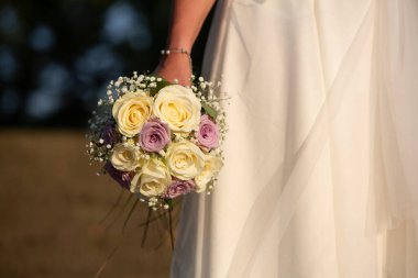 Gelin, düğün gününde elinde güzel bir buket beyaz ve mor gül tutuyor.