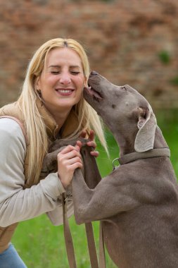 Kadın Weimaraner köpeğini kucaklarken gözleri kapalı gülümsüyor.