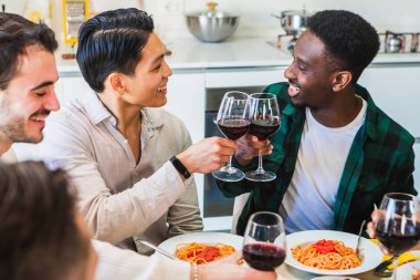 Bir grup arkadaş mutfakta makarna yerken gülümsüyor ve eğleniyorlar.