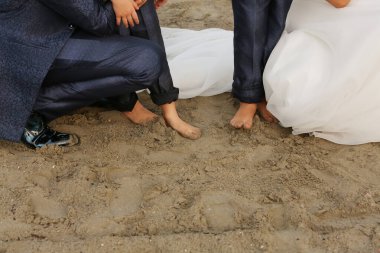 Gelin ve damat sahilde diz çöküp çıplak ayaklarını gösteriyorlar.