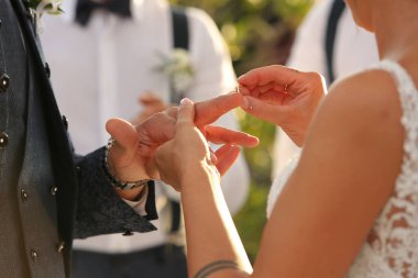 Gelin, açık havada yapılan güzel bir düğün töreninde damadın parmağına yüzük takıyor.