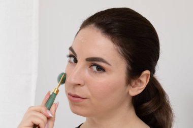 Genç bir kadın, yaşlanmayı ve cilt bakımını önlemek için yüzüne yeşim bir silindir takıyor.