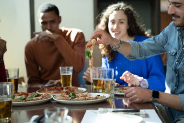 Bir grup arkadaş pizza ve biranın tadını çıkarıyor, birlikte bir restoranda öğle yemeği yiyorlar.