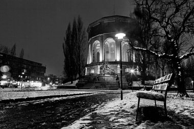 Siyah ve beyaz gece fotoğrafçılığı neoklasik bir anıtı aydınlatan kar kaplı bir bank sergiliyor.