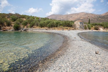 Turkuaz suları ve terk edilmiş taştan bir evi olan gözlerden uzak bir Yunan çakıl taşı plajı.