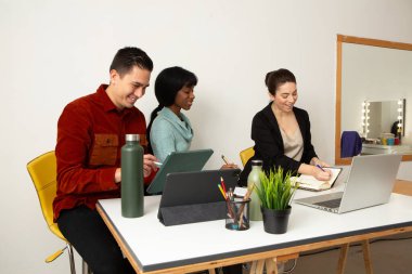 Üç girişimci bir proje üzerinde birlikte çalışıyor, notlar alıyor ve gülümsüyor.