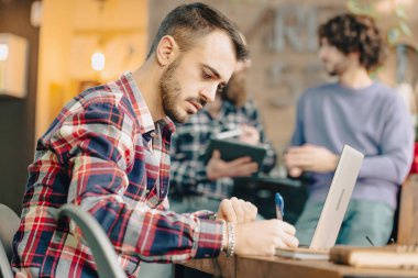 Genç adam iş arkadaşlarıyla yaptığı bir toplantıda not defterine not alıyor.