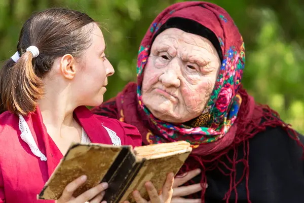 stock image Young actress is rehearsing her role with a senior woman holding an old book in a park