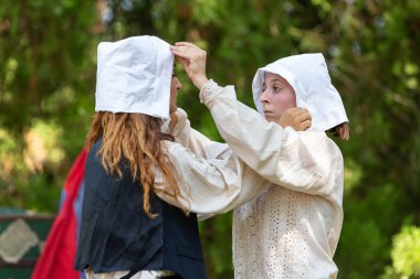 İki kadın beyaz şapkalarını düzeltip 16. yüzyıldaki hayatı resmetmeye hazırlanıyorlar.