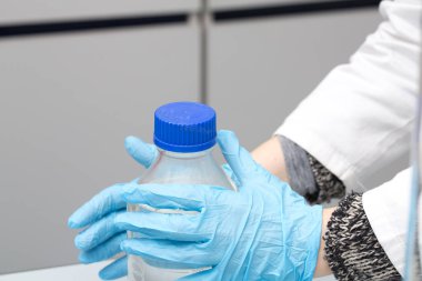 Bilim adamı laboratuvar ortamında mavi eldivenli bir laboratuvar şişesi tutuyor.