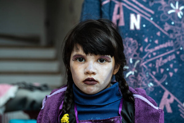 Young girl with dark braided hair and purple halloween makeup is posing indoors