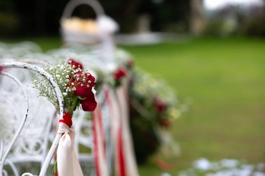 Kırmızı güller ve bebek nefesi beyaz düğün sandalyelerini süslüyor, açık hava törenine biraz zarafet katıyor.
