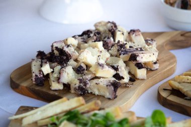 Kül kaplamalı peynir parçaları, ahşap bir kesme tahtasına dizilmiş, açık büfede ya da yemek servisinde servis edilmeye hazır.