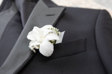 Damadın zarif siyah takım elbisesine yakın plan, beyaz çiçekli yaka çiçeği, düğün günü aşkı ve kutlamayı simgeliyor.