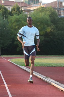 Genç atletik bir adam açık alanda koşuyor.