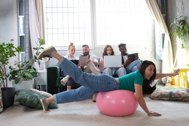 Meslektaşları bilgisayarları ve tabletleri üzerinde çalışırken modern bir ofiste spor yapan bir kadın.