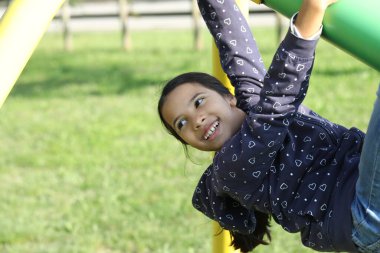 Oyun parkında baş aşağı asılı gülümseyen kız dışarıda oyun oynamaktan hoşlanıyor.