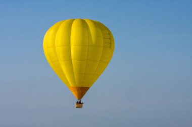 Açık mavi gökyüzüne doğru yükselen parlak sarı sıcak hava balonu, serüvenin ve seyahatin huzurlu bir görüntüsünü sunuyor.