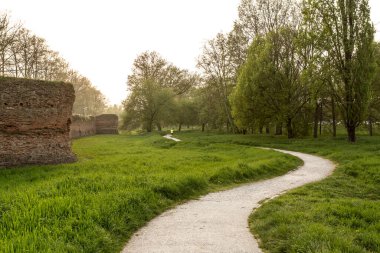 Huzurlu günbatımı, bereketli yeşil bir parktaki antik Roma duvarlarının yanında dolambaçlı bir çakıl yolunu aydınlatır. Tarihe ve doğaya huzurlu bir kaçış sunar.