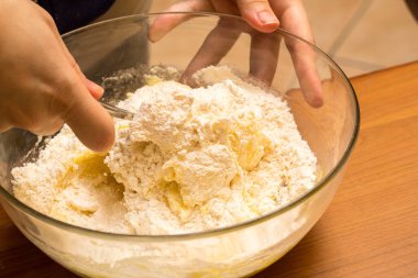 Elleri hamuru cam bir kasede çatalla karıştırarak pişirmek için gerekli malzemeleri hazırlıyor.