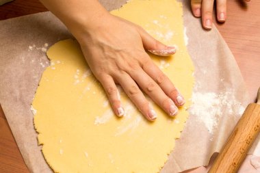 Kadın hamuru kabartma kağıdına yassıyor, kurabiye veya bisküvi yapmaya hazırlanıyor.