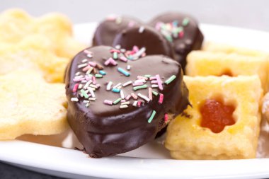 Lezzetli kalp şeklinde çikolatalı kurabiye. Etrafı beyaz bir tabakta diğer kurabiyelerle çevrili.