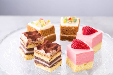 Cam bir tabağa dizilmiş renkli mini keklerin çeşitliliği bir pasta şefinin beceri ve yaratıcılığını gözler önüne seriyor.