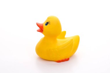 Klasik sarı plastik ördek oyuncağı el değmemiş beyaz bir arka planda yüzüyor, çocukluk anılarını ve masumiyeti çağrıştırıyor.