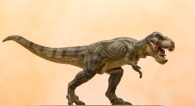 Plastik Tyrannosaurus Rex oyuncağı turuncu arka planda kükreyen ve iki ayak üzerinde yürüyen