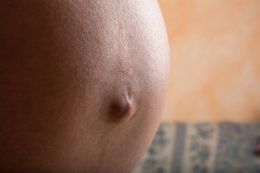 Hamile bir karna yakın plan, çıkıntılı göbek ve deri dokusunu vurguluyor.