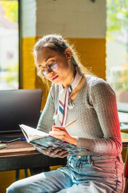 Kafede çalışırken not defterine not alan odaklanmış kız öğrenci.