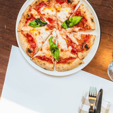 Eritilmiş mozzarella peyniri ve fesleğen yapraklı dilimlenmiş pizza margherita, ahşap bir restoran masasında servis edilir.