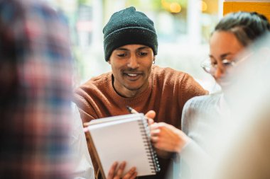 Üniversite öğrencileri bir proje üzerinde işbirliği yapıyorlar, notlarını paylaşıyorlar ve bir kafede birlikte okuyorlar.