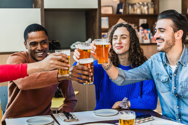 Cheerful multi-ethnic friends toasting with beer glasses while enjoying time together at brewery restaurant