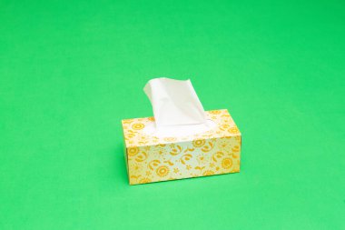 Çiçek desenli bir dokuma kutusu canlı yeşil bir zemine beyaz dokular dağıtır.